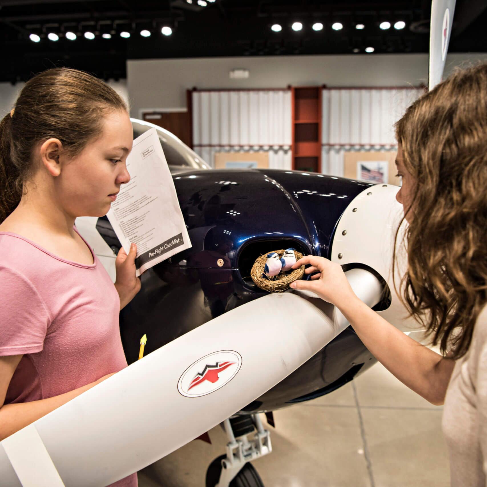 Two girls examine a model bird's nest placed near the propellers of an airplane during a workshop to earn a Girl Scout patch hosted at the Lone Star Flight Museum in Houston, TX.
