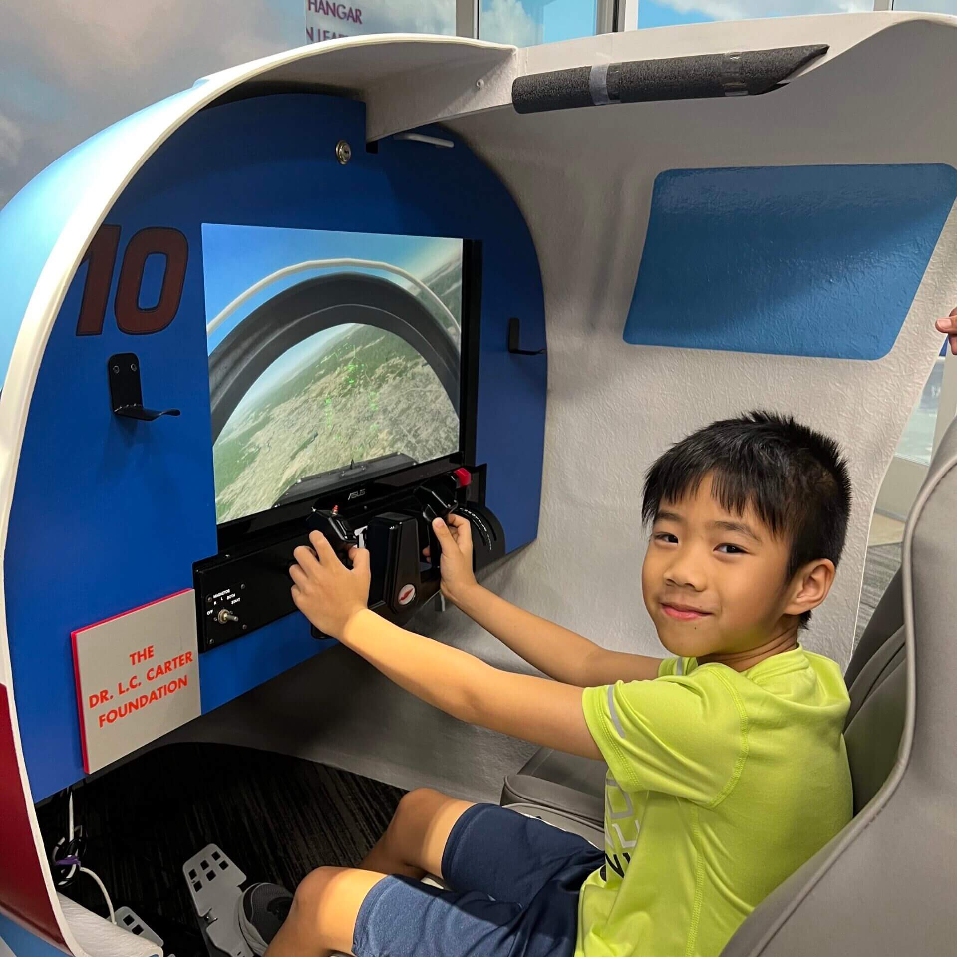 A boy smiles as he uses the flight simulator available to participants of the summer camp programs hosted at the Lone Star Flight Museum in Houston, TX.
