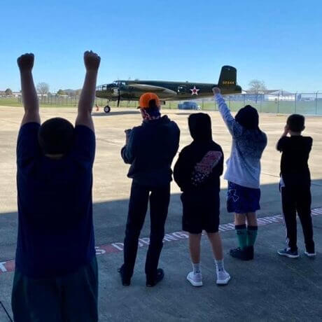 Kids cheer as an airplane passes in front of them during a summer camp program hosted at the Lone Star Flight Museum in Houston, TX.